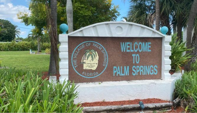 A welcome to palm springs sign is surrounded by palm trees
