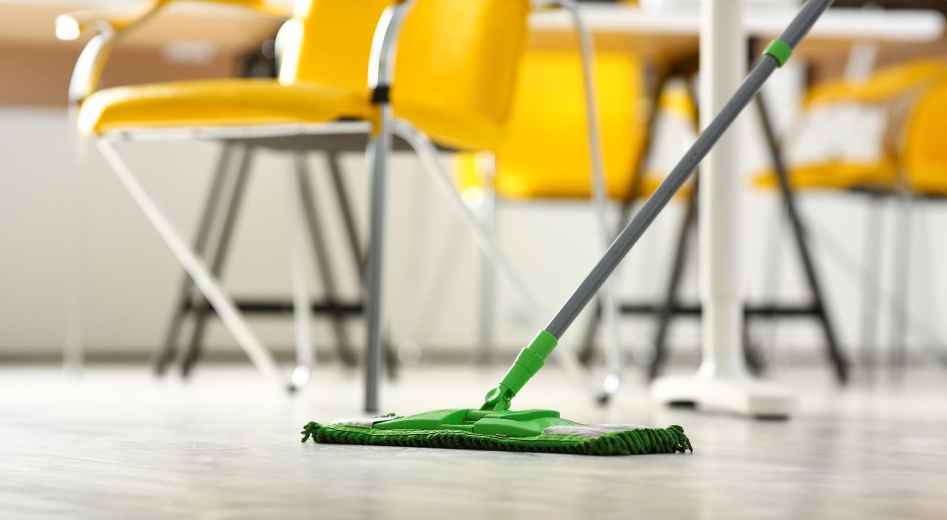 A green mop is sitting on a wooden floor in an office.