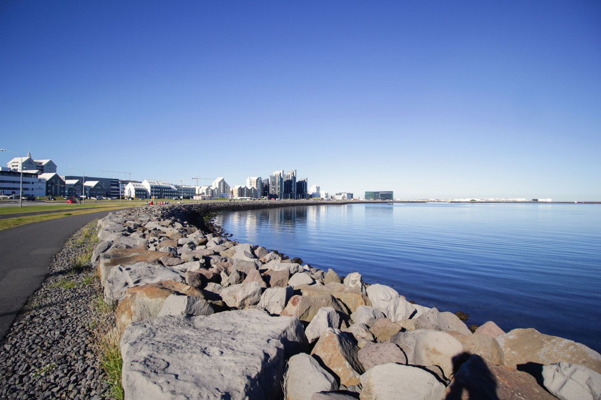 A large body of water with rocks on the shore and a city in the background.