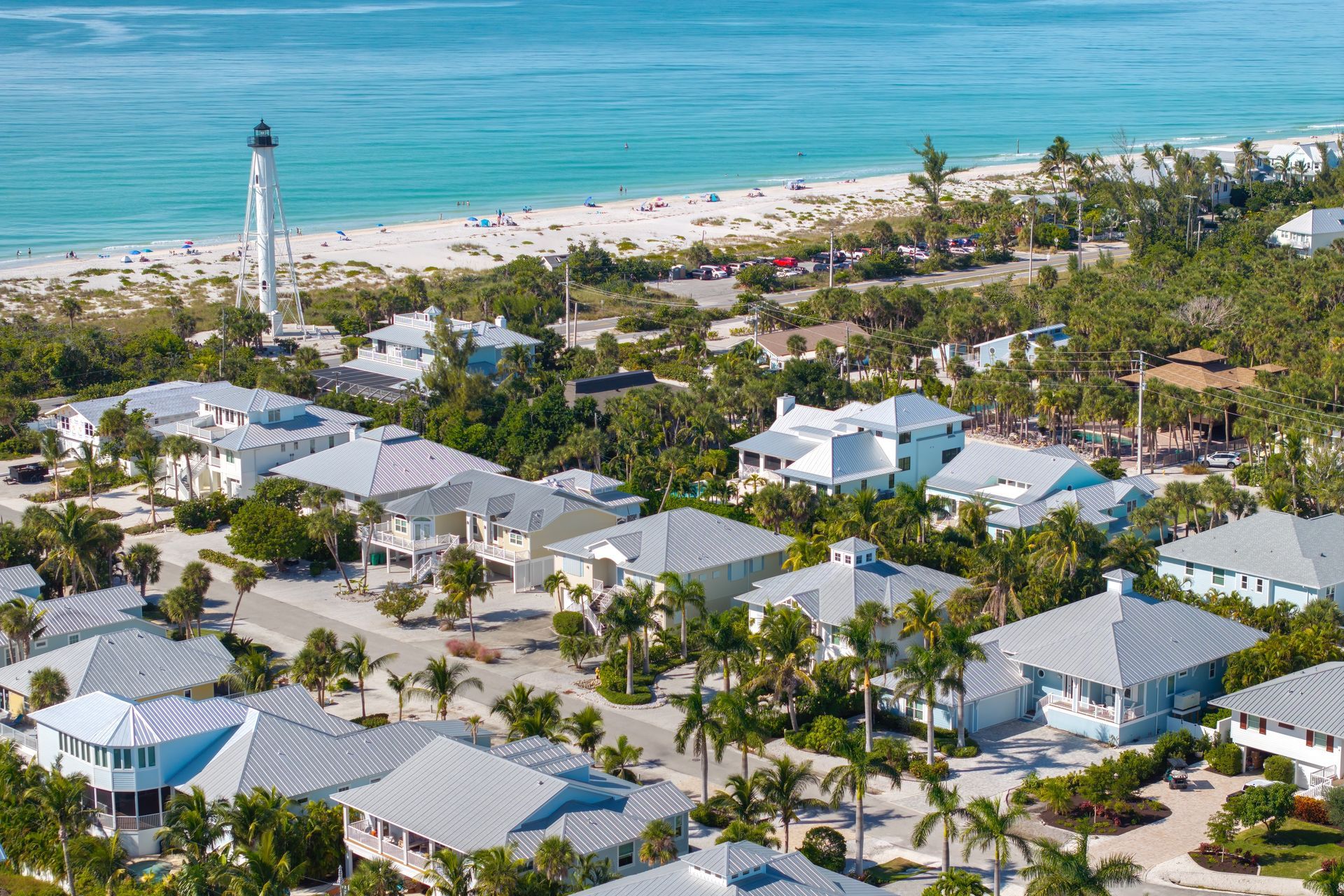 An aerial view of a residential area next to the ocean with a lighthouse in the background.